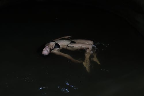 Free A woman in a bikini floats serenely in dark, calm water, capturing a moment of relaxation. Stock Photo