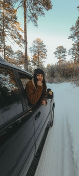 Young woman looking out a car window during a winter road trip through a snowy forest.