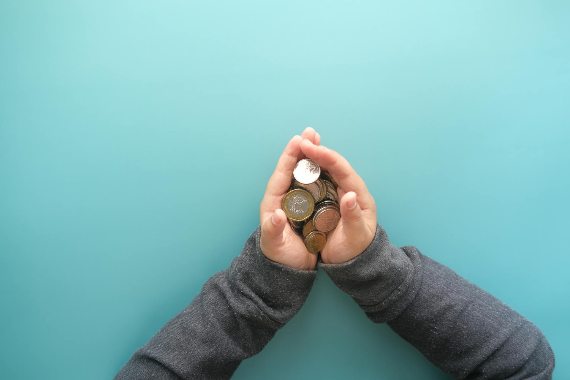 Two hands holding a stack of coins against a blue background, symbolizing savings or financial security.