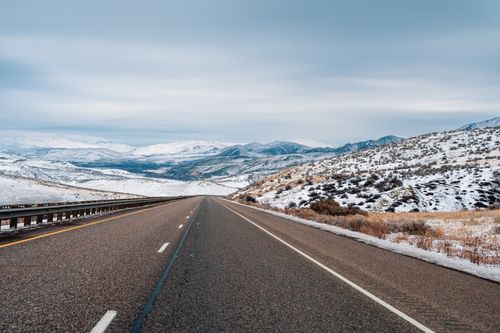 Free Empty highway running through snow-covered mountains under a cloudy winter sky. Stock Photo
