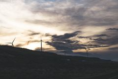 Silhouette of wind turbines on a hill with a dramatic cloudy sky at sunset.