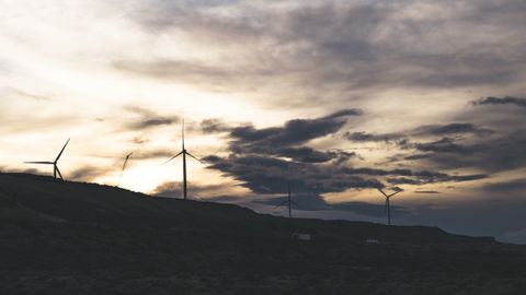 Silhouette of wind turbines on a hill with a dramatic cloudy sky at sunset.