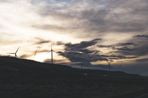 Free Silhouette of wind turbines on a hill with a dramatic cloudy sky at sunset. Stock Photo