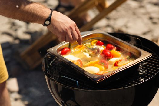 Close up of person cooking vibrant vegetables with cheese on an outdoor grill.