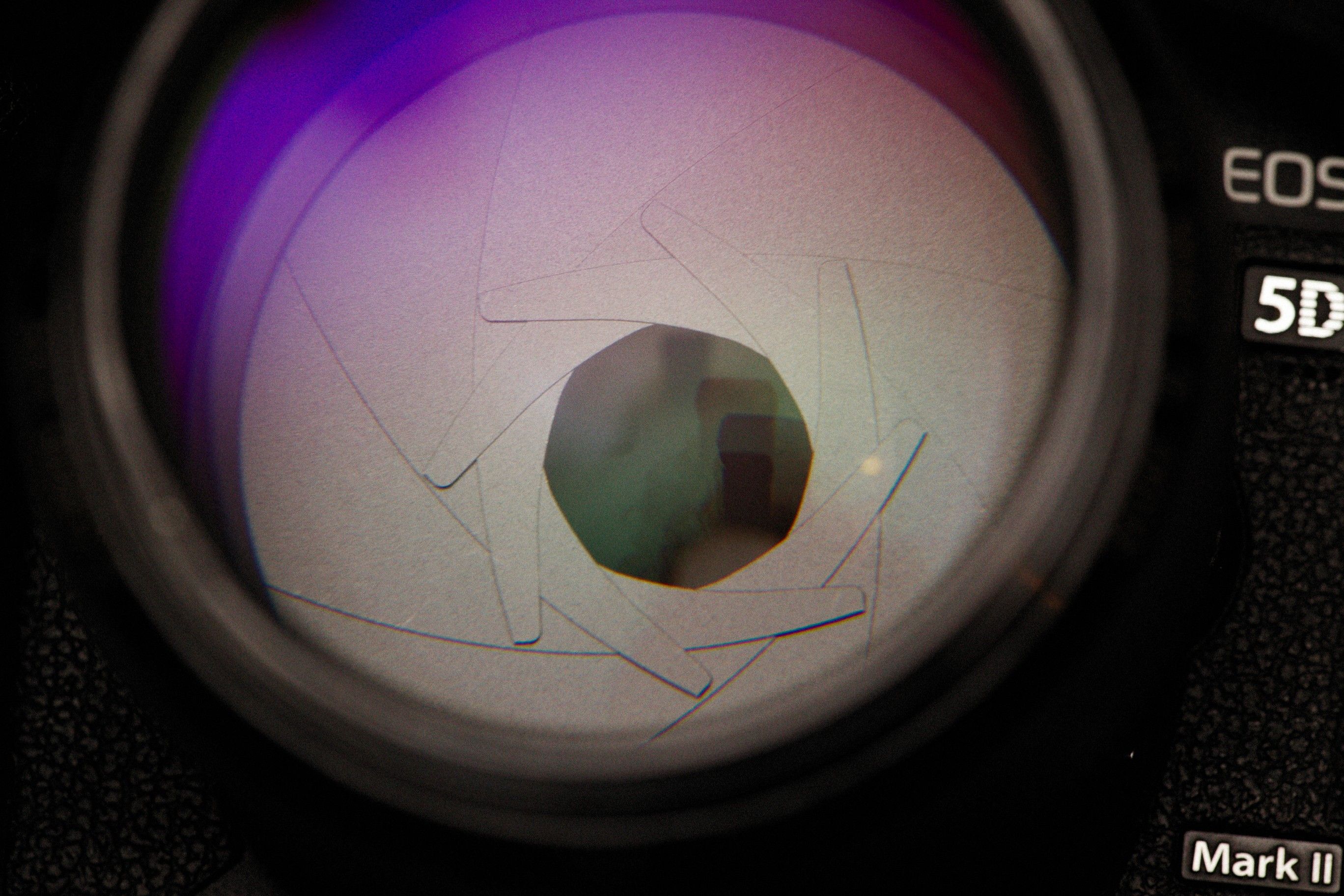 Detailed close-up of a camera lens showing aperture blades with colorful reflections.