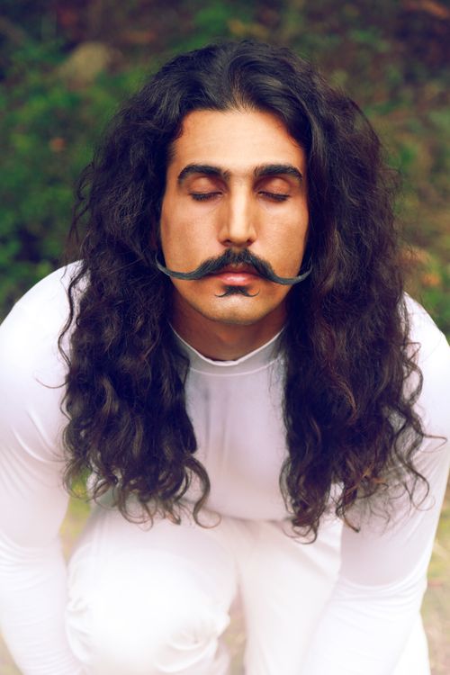 Free Portrait of a man with long hair and mustache in a white outfit, eyes closed peacefully outdoors. Stock Photo