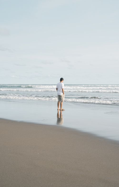 Free A man walking along a tranquil beach in Indonesia. Calm waves and clear sky. Stock Photo