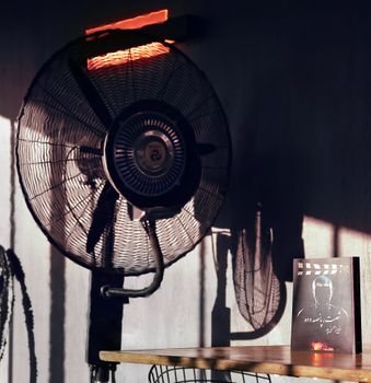 Cozy room with a book and electric fan casting dramatic shadows.