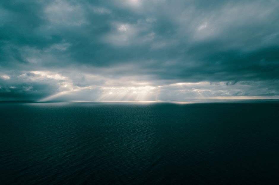 Sunbeams break through dramatic clouds over a vast ocean, creating a stunning seascape view.