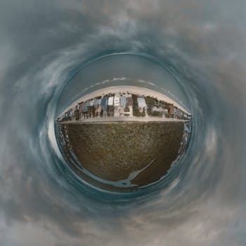 Unique aerial 'small planet' perspective showing a coastal neighborhood with surrounding landscape and sky.