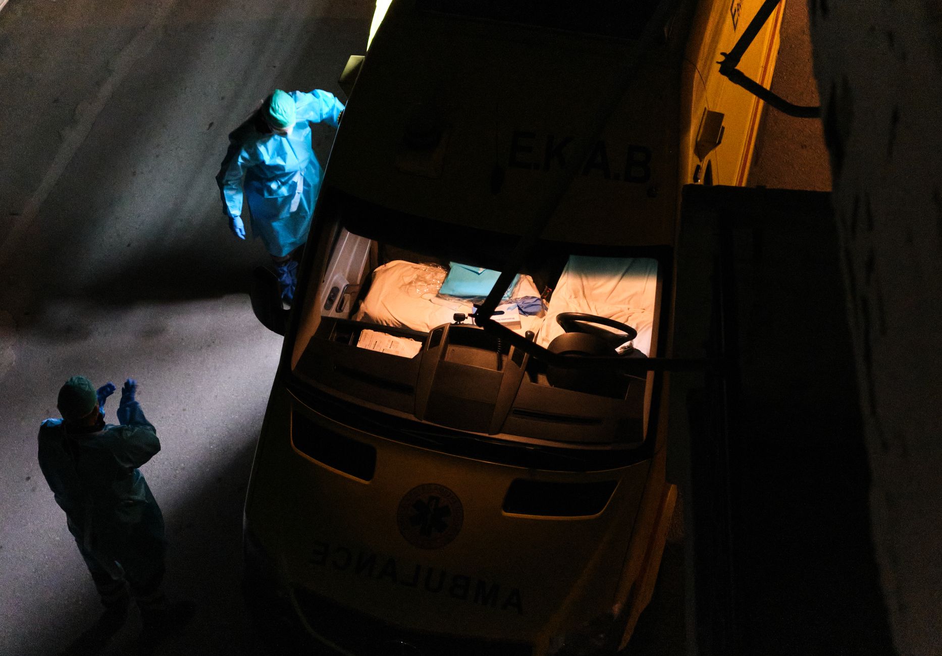 Aerial view of medical personnel in hazmat suits attending an ambulance at night.