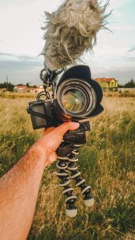 Close-up of a DSLR camera with microphone in a grassy field on a cloudy day, emphasizing outdoor vlogging setup.
