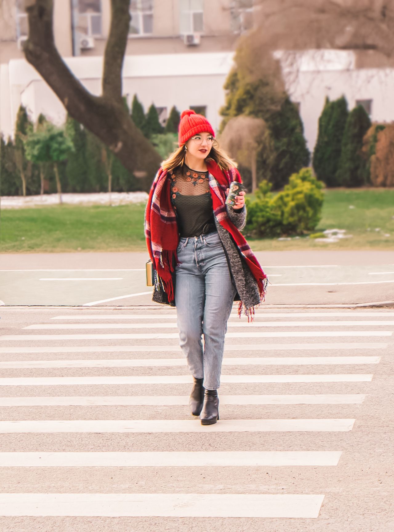 Woman in a red beanie, plaid shawl and jeans crossing a street