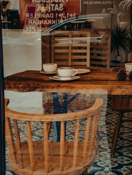 Cozy coffee shop interior with wooden chairs and table, featuring cups of coffee and warm reflections.