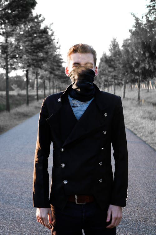 Young man standing on alley in park in and exhaling steam through black mask