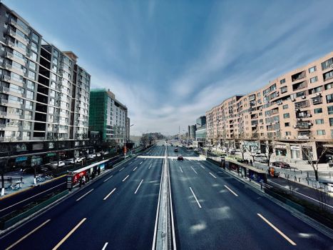 Wide urban road with surrounding buildings under a clear blue sky.