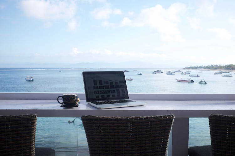 A Laptop On A Table Near Glass Windows With The Sea View