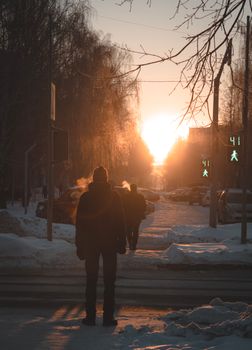 Early morning winter scene with people walking on a snowy street during sunrise.