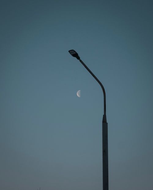 Free A low-angle view of a streetlight set against a serene blue sky with a visible half moon. Stock Photo