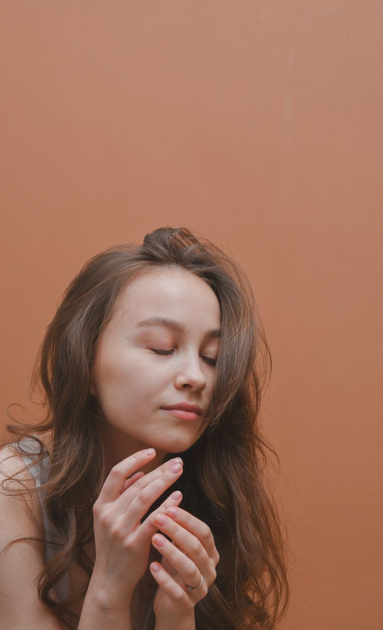 Serene portrait of a woman with long wavy hair and closed eyes against a soft background.