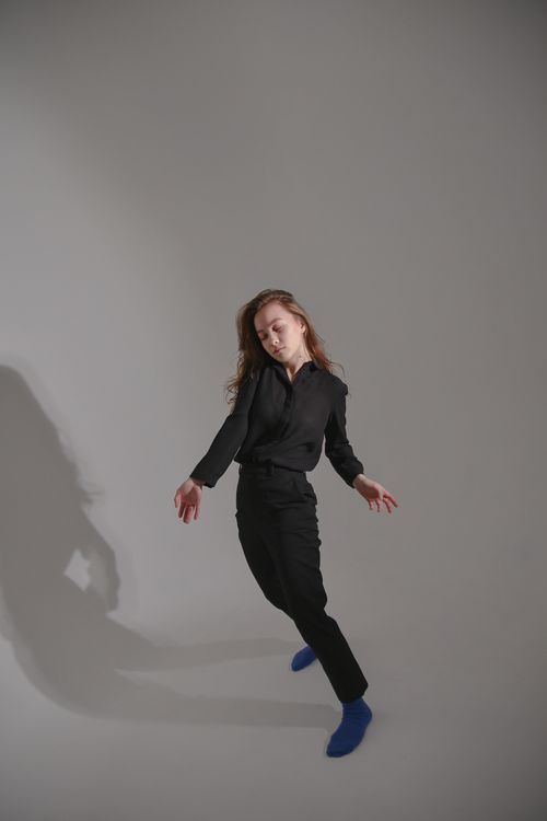 Free Young woman in a dynamic dance pose wearing a black outfit against a gray studio backdrop. Stock Photo