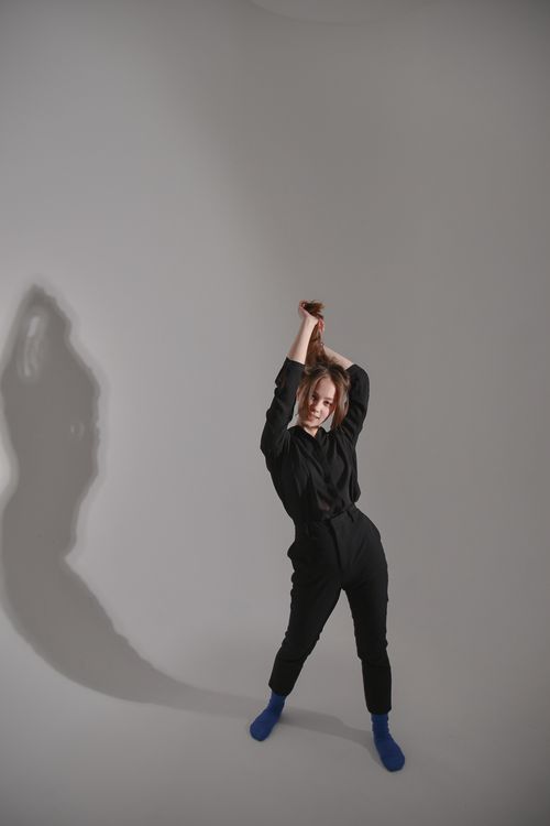 Free Artistic studio shot of a woman posing with hands overhead in black attire. Stock Photo