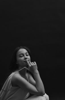 A serene black and white portrait of a woman relaxing in a spaghetti strap dress with eyes closed.