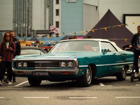 Classic blue vintage car on display at an urban event with a crowd.
