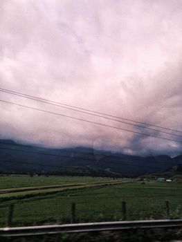 A dramatic stormy sky looms over lush fields with a distant mountain range.