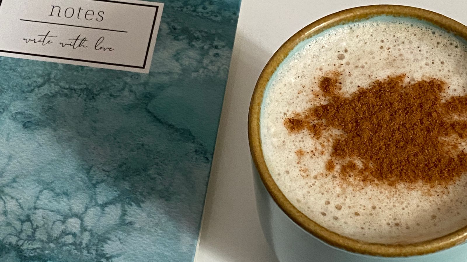 A cup of coffee beside a blue notebook on a table