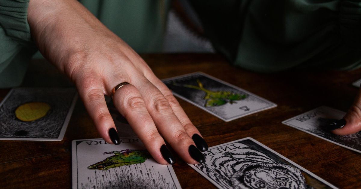 A reader's hand drawing a single card from a tarot spread on a dark wooden table, the one-card pull at the heart of a daily tarot reading
