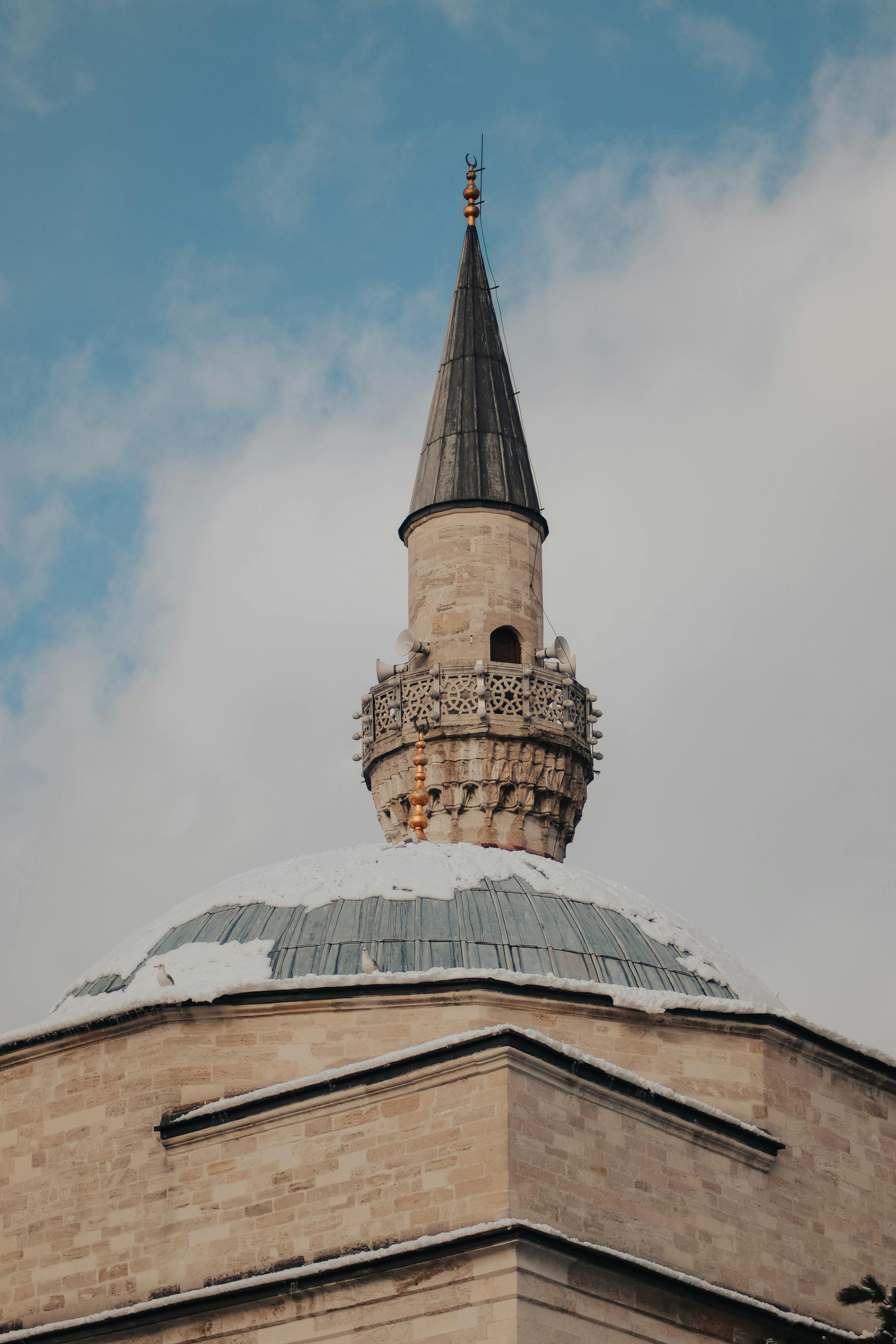 Low angle shot of a mosque's minaret and dome with snow, under a clear sky.