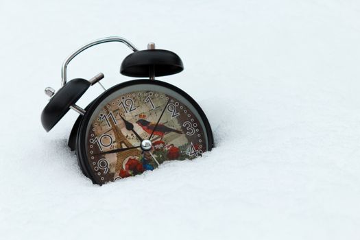 A vintage alarm clock with an Eiffel Tower design partially buried in snow, capturing a winter theme.