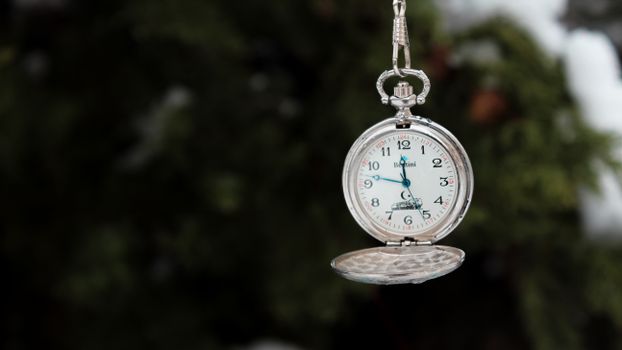 Close-up of a silver pocket watch hanging with blurred natural background.