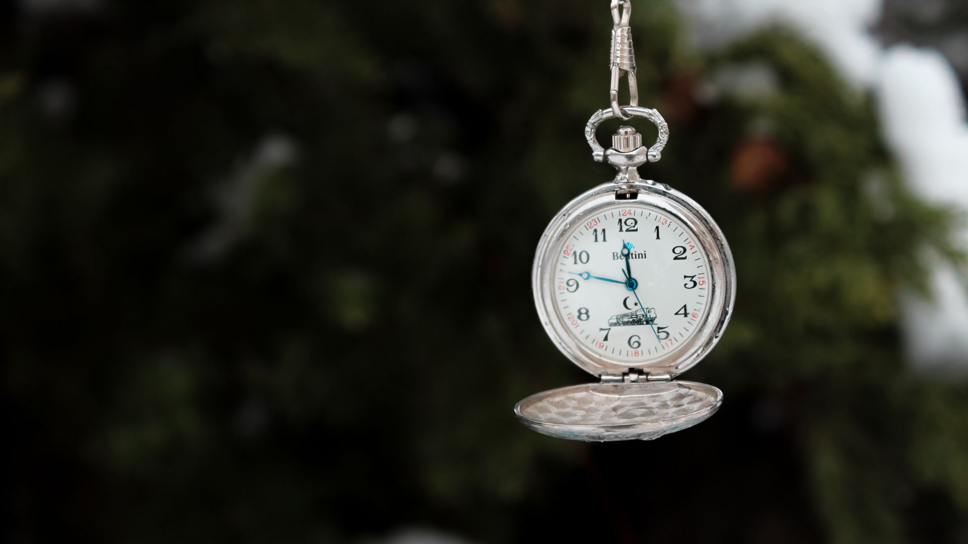 Close-up of a silver pocket watch hanging with blurred natural background.