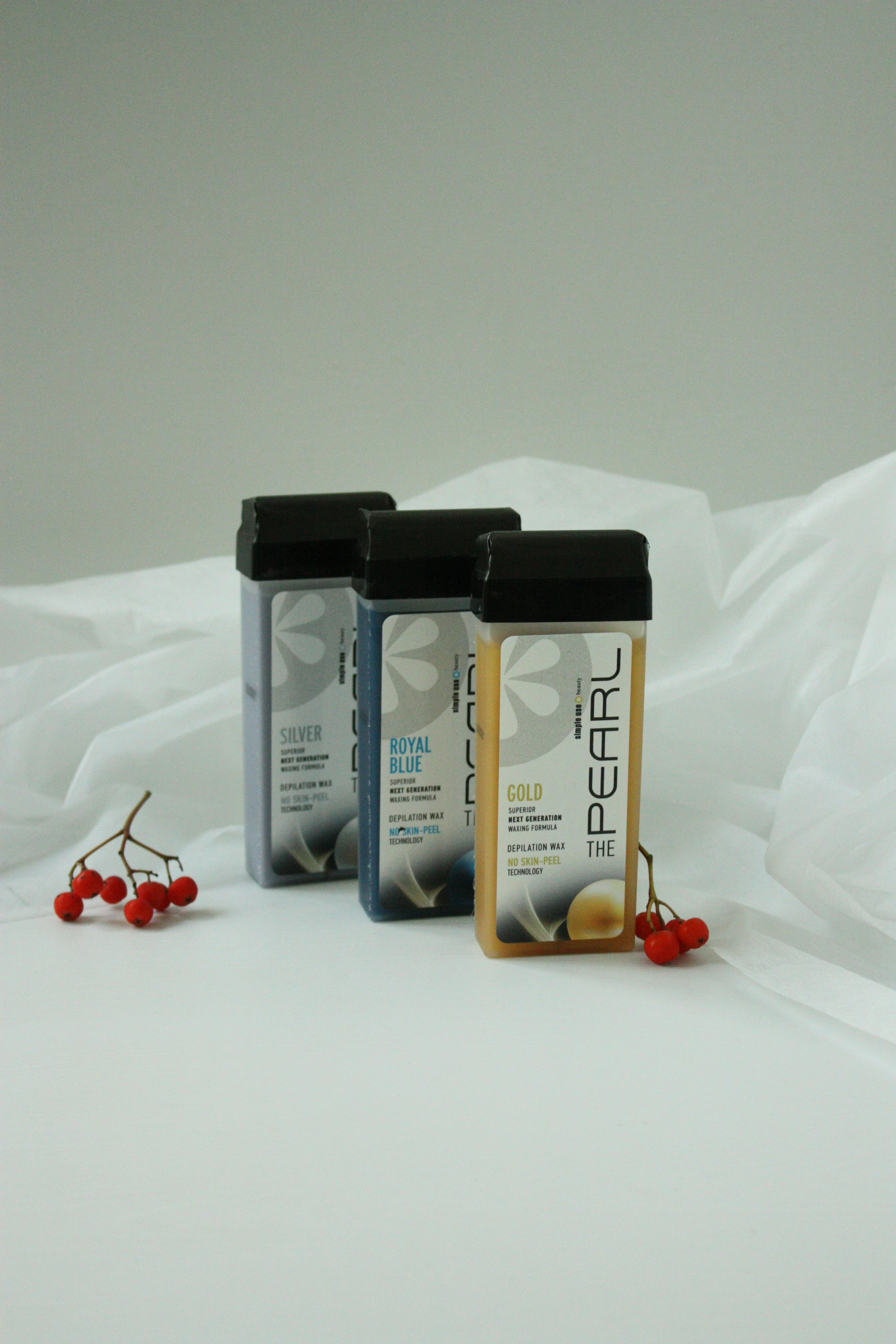 Aesthetic shot of three roll-on wax bottles with red berries on white fabric, creating a minimalist vibe.