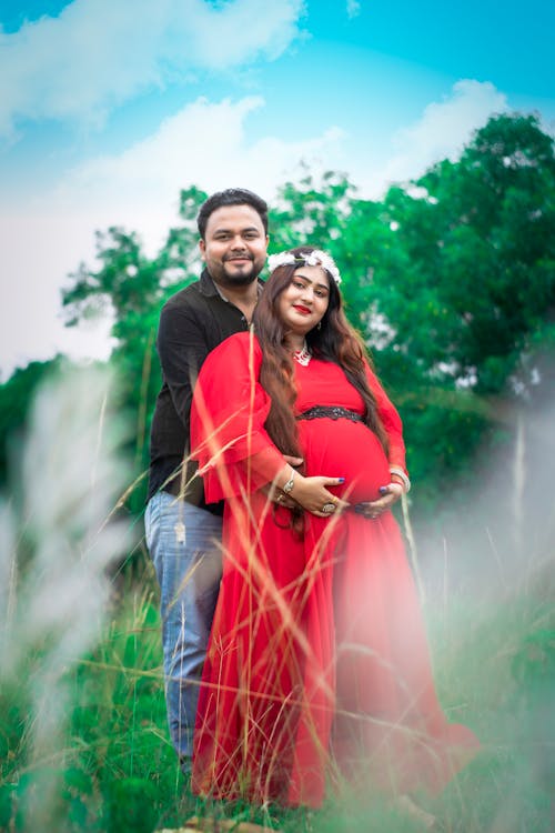 A Pregnant Woman in Red Dress Hugged By Her Partner