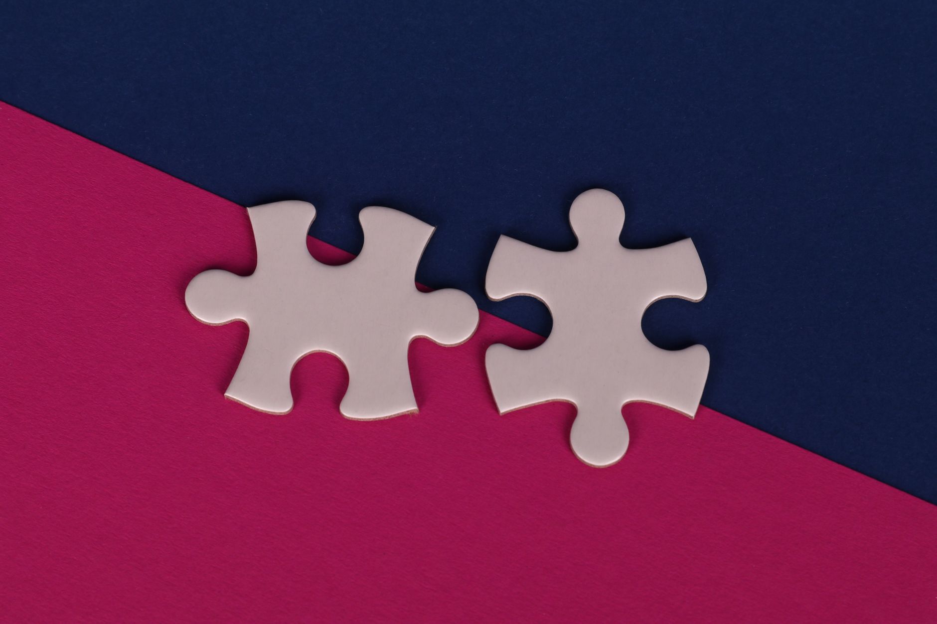 Close-up of white puzzle pieces on bold pink and navy background.