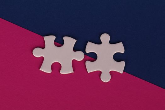 Close-up of white puzzle pieces on bold pink and navy background.