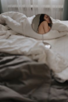 Artistic shot of a woman's reflection in a mirror amidst bed sheets.