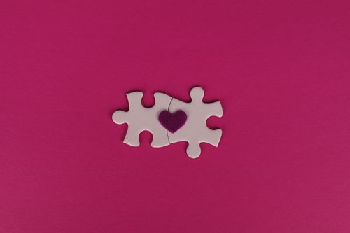 Free Two white puzzle pieces with a heart symbol on a pink background, symbolizing love and connection. Stock Photo