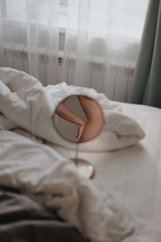 A creative composition featuring a woman's arm reflected in a mirror placed on a bed.
