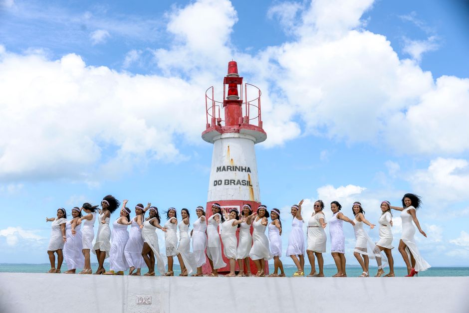 Women in white dresses celebrate by a lighthouse in Brazil.
