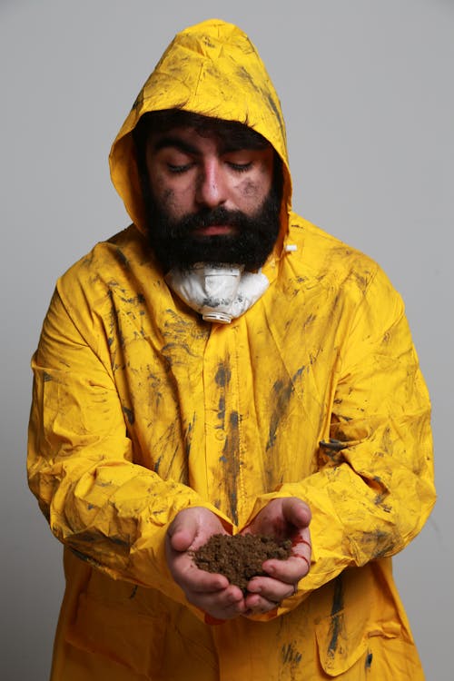 Man in Muddy Yellow Raincoat Holding Soil in his Hands 