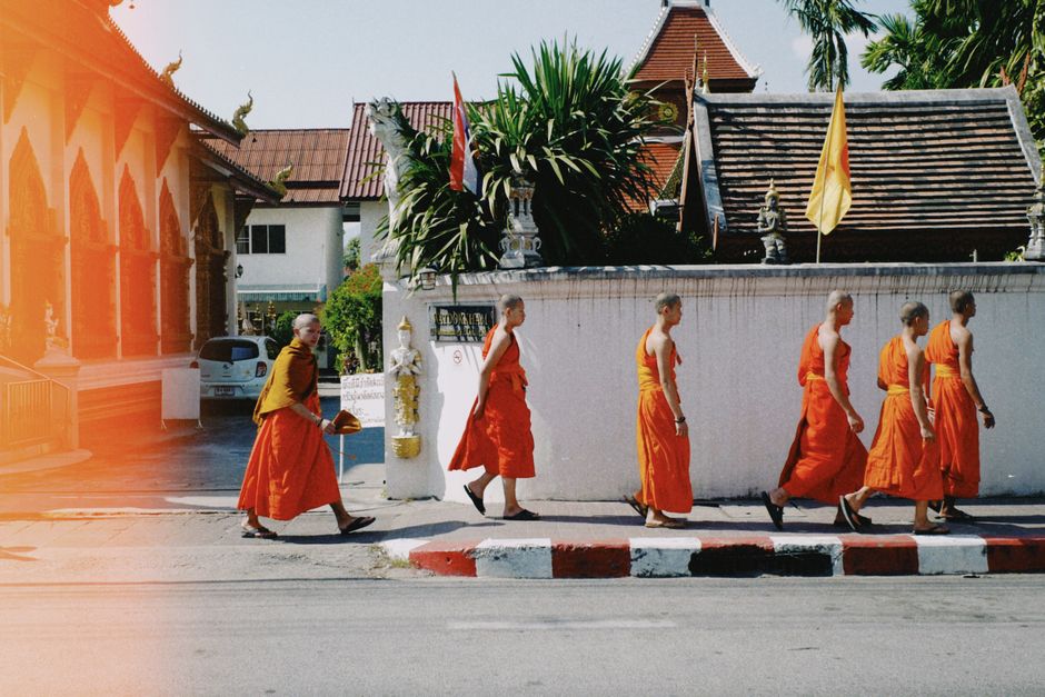 Buddhist monks in orange robes walk along a temple wall in daylight, creating a serene scene.