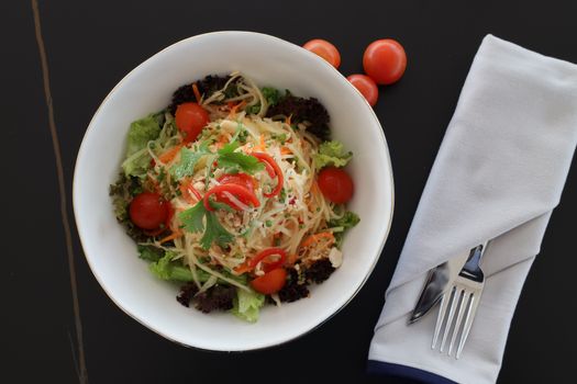 Top view of a fresh vegetable salad with cherry tomatoes and herbs on a black background.