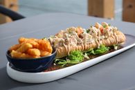 Savor a delicious lobster roll drizzled with sauce and crispy fries on the side, perfect for a gourmet meal.