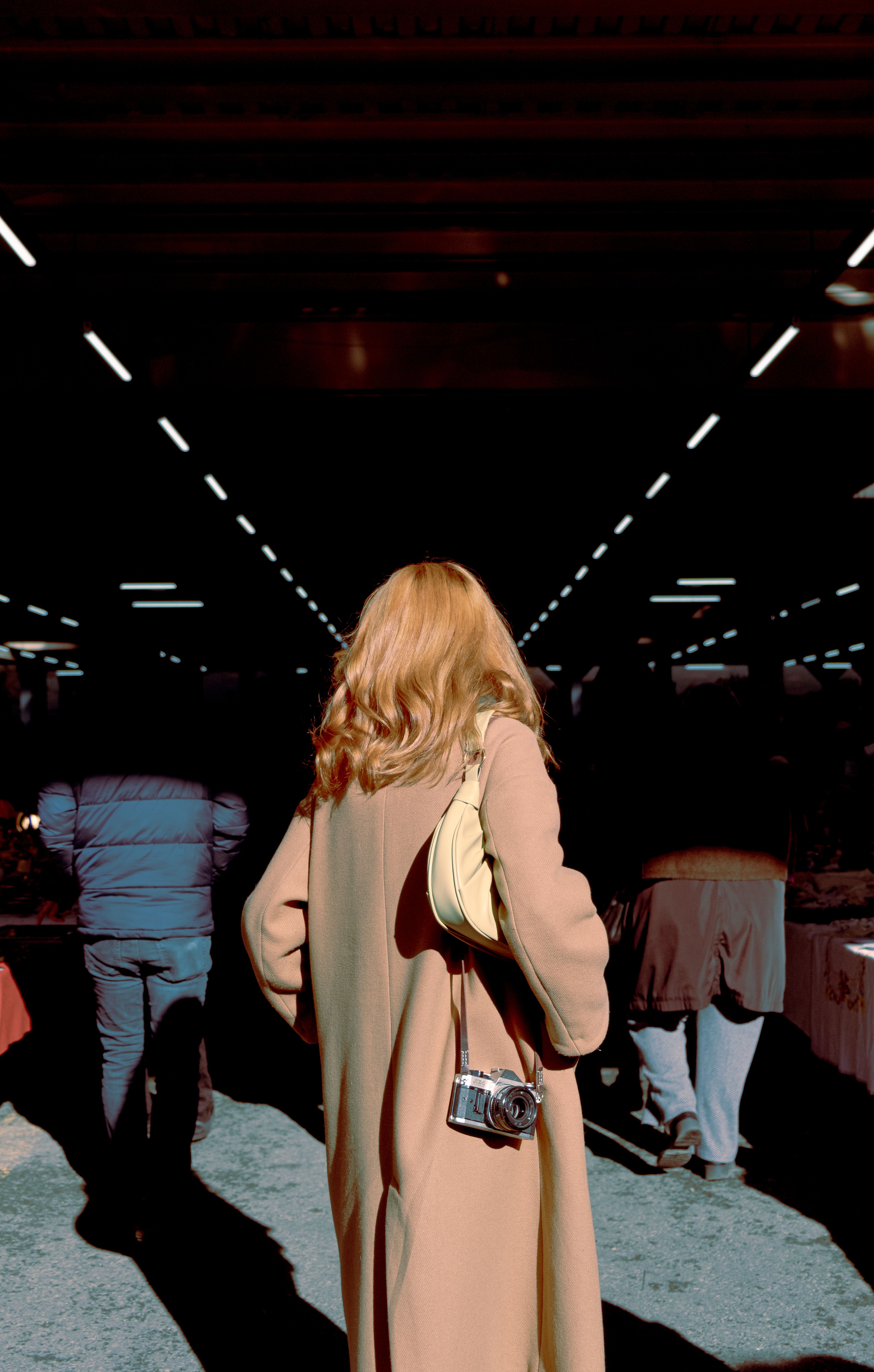 Blonde woman in an elegant coat walking outdoors in sunlight, showcasing urban fashion.