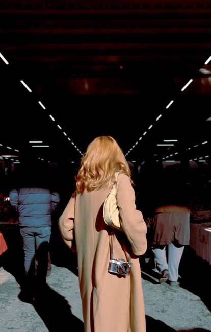 Blonde woman in an elegant coat walking outdoors in sunlight, showcasing urban fashion.
