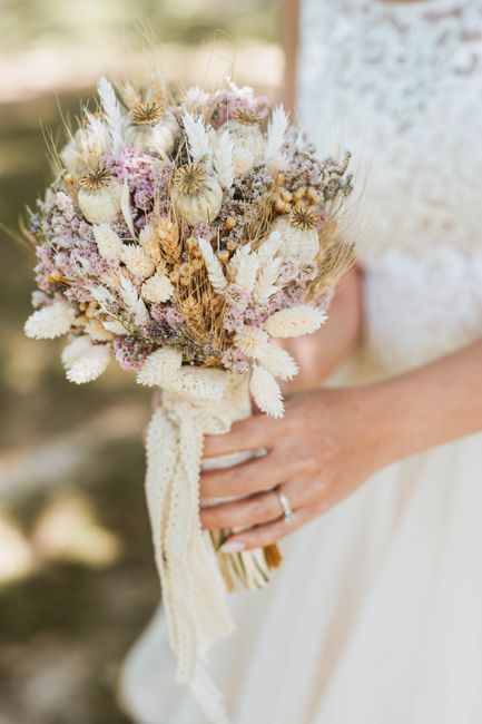 A close-up of a bride holding a rustic dried flower bouquet in natural sunlight.